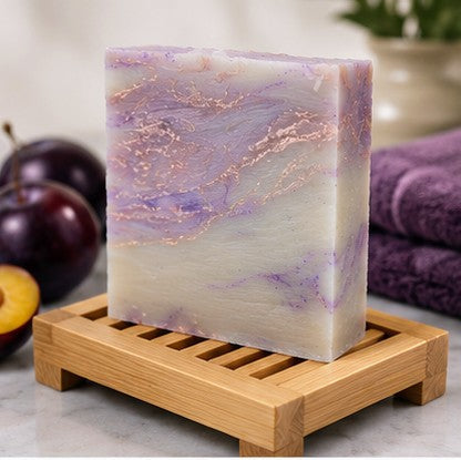 Plum sugar soap bar on wooden dish with fresh plums